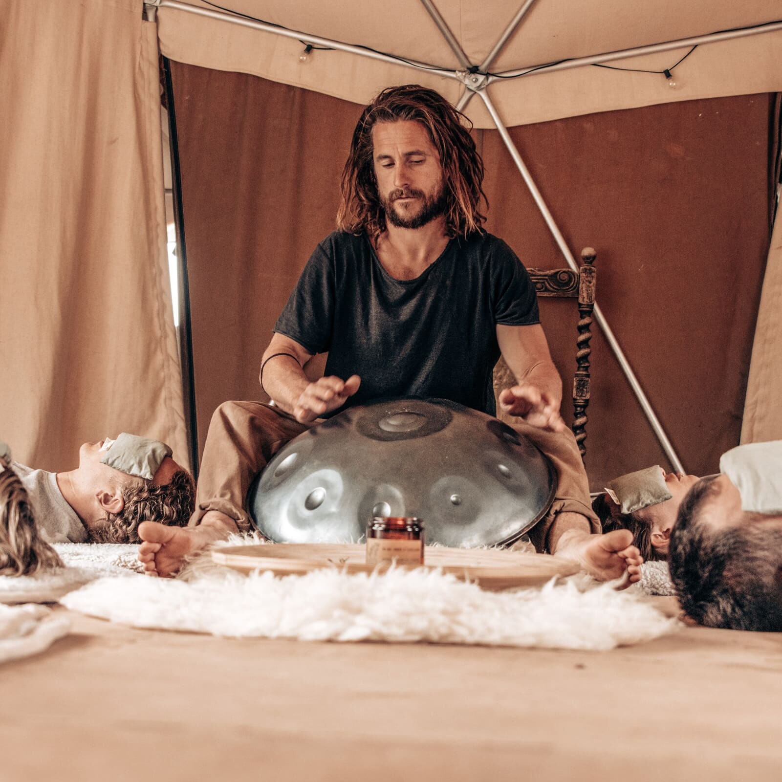 Practitioner playing a handpan during a Soul Sweats sound healing session, surrounded by participants lying with eye pillows in a calm tented space.