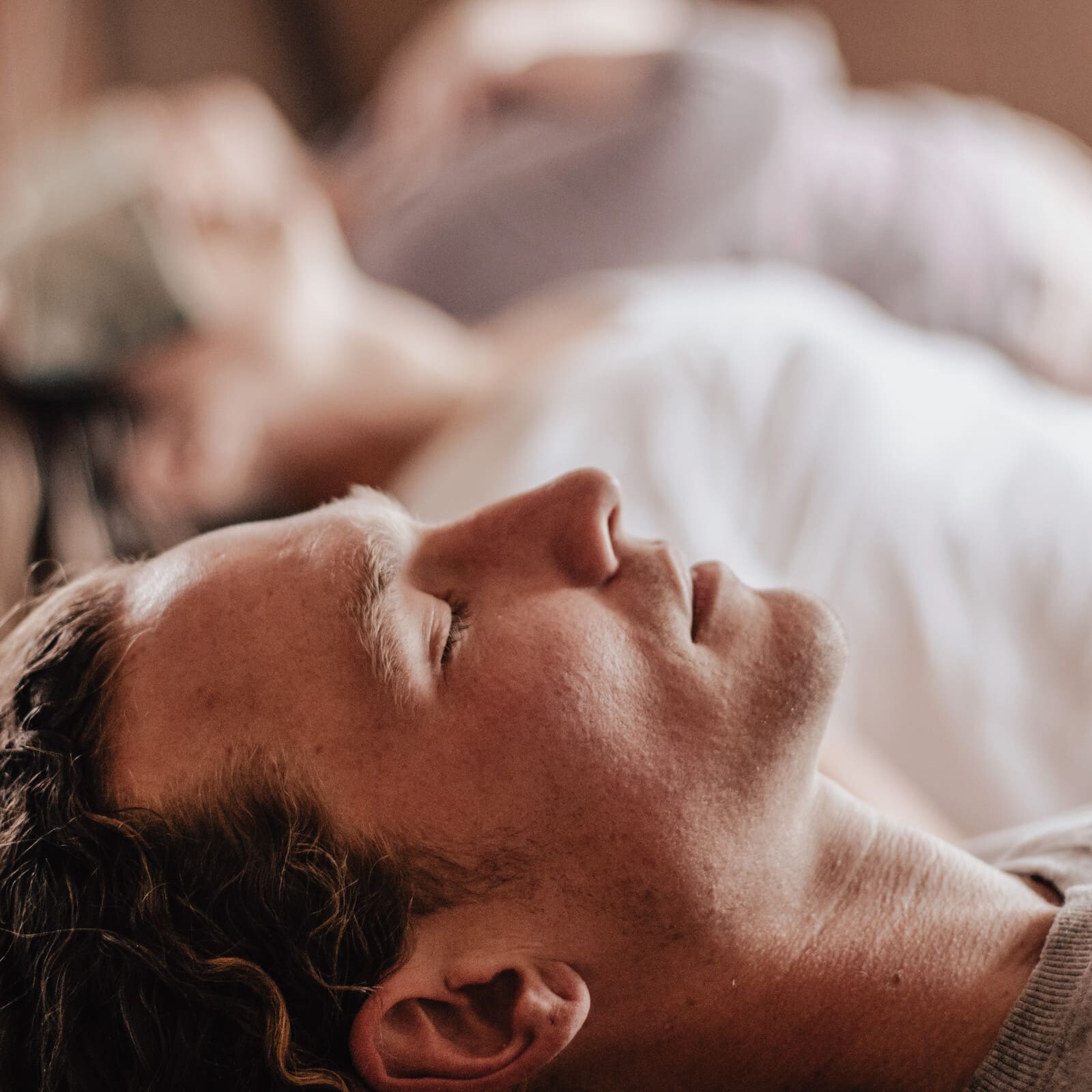 Man lying down with eyes closed during a Soul Sweats holistic health session, relaxing while others rest in the background.