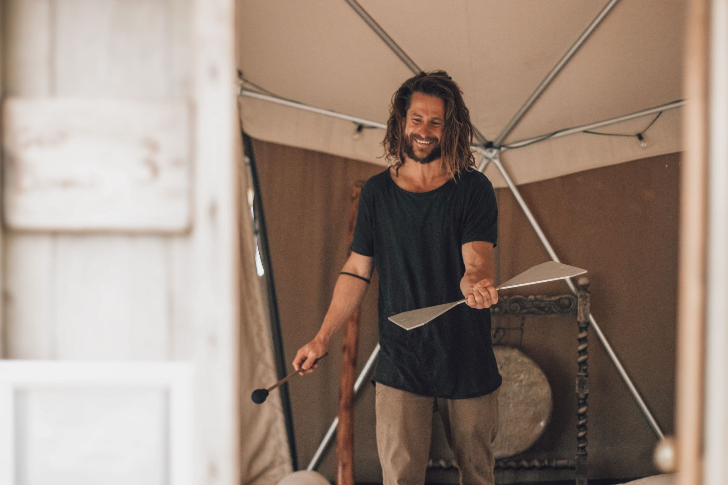 Practitioner leading a Soul Sweats holistic health session, smiling while holding tuning forks inside a calming tented space.