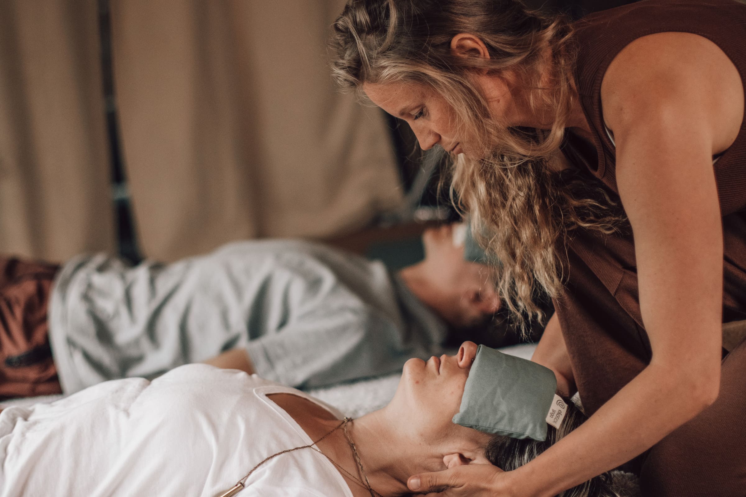 Practitioner supporting a client during a Soul Sweats holistic healing session, gently placing an eye pillow as they relax on a mat.