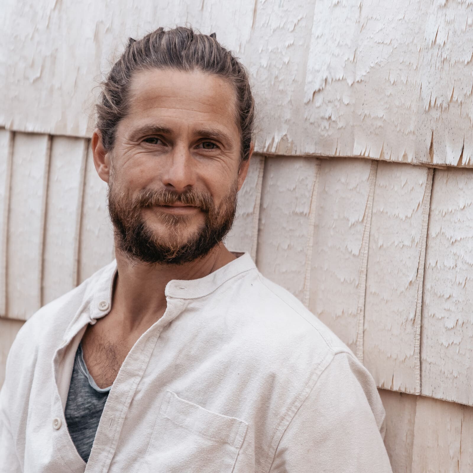 Portrait of Sam, owner of Soul Sweats, smiling in natural light against a textured wooden wall.