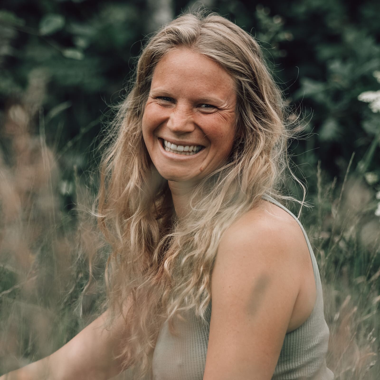 Portrait of Jana, co-owner of Soul Sweats, smiling outdoors among tall grass and soft natural greenery.