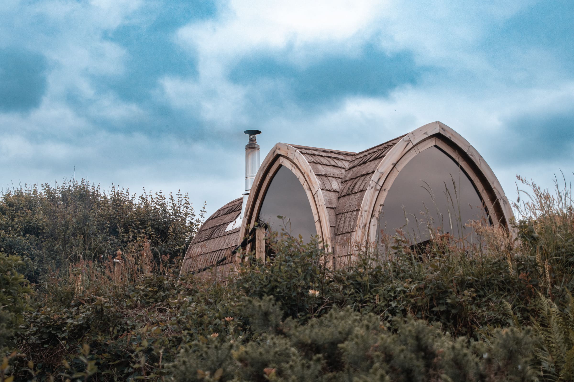 Soul Sweats wild sauna at Mount Pleasant Eco Park, nestled in tall coastal grasses beneath a dramatic blue sky.