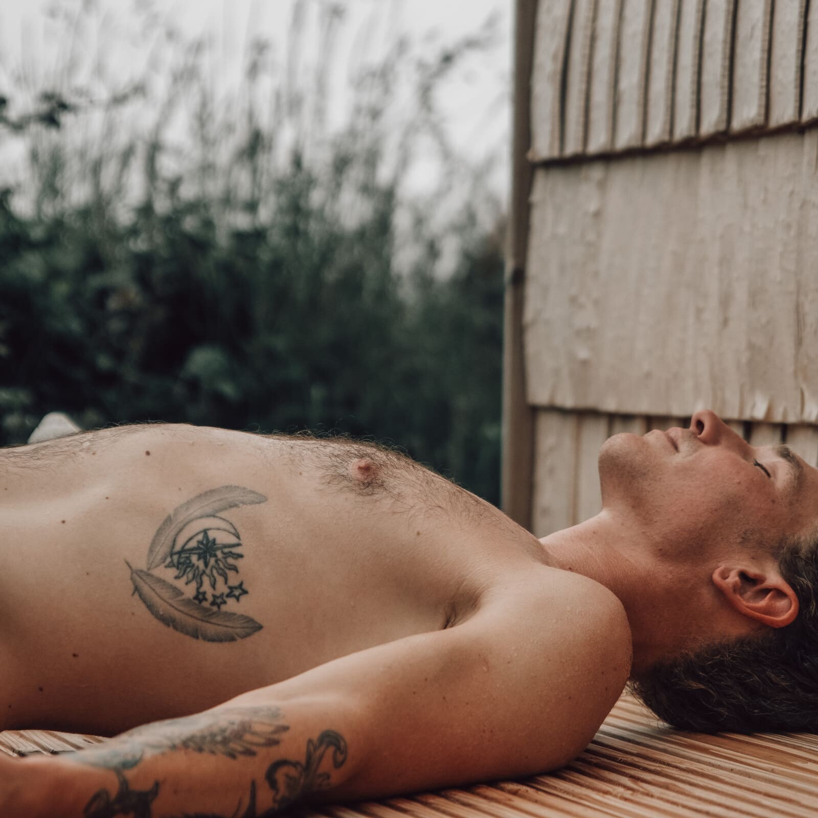 Man resting on wooden decking outside the Soul Sweats sauna, lying in the warm sunlight with greenery in the background.